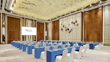 A conference room with rows of tables and chairs, a large screen, and a decorative ceiling.