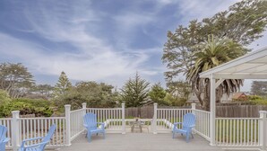 A covered deck with blue Adirondack chairs and a small table, surrounded by white railings and a wooden fence. - 3828 The 9th Green - Near Golf Links & Bay Trail (Pacific Grove)