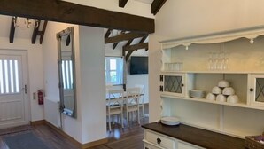 A kitchen with wooden flooring, white cabinetry, and a dining area with a table and chairs. - The Estate - 11 Bed - Sleeps 22 - Private Garden (Hailsham)