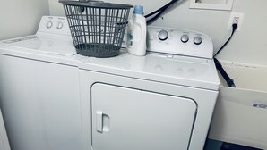 Une machine à laver blanche à chargement frontal, avec une bouteille de lessive et un panier à linge posé sur le dessus.