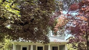 Une maison à deux étages avec un porche à l’avant, un petit jardin et un chemin menant à l’entrée.