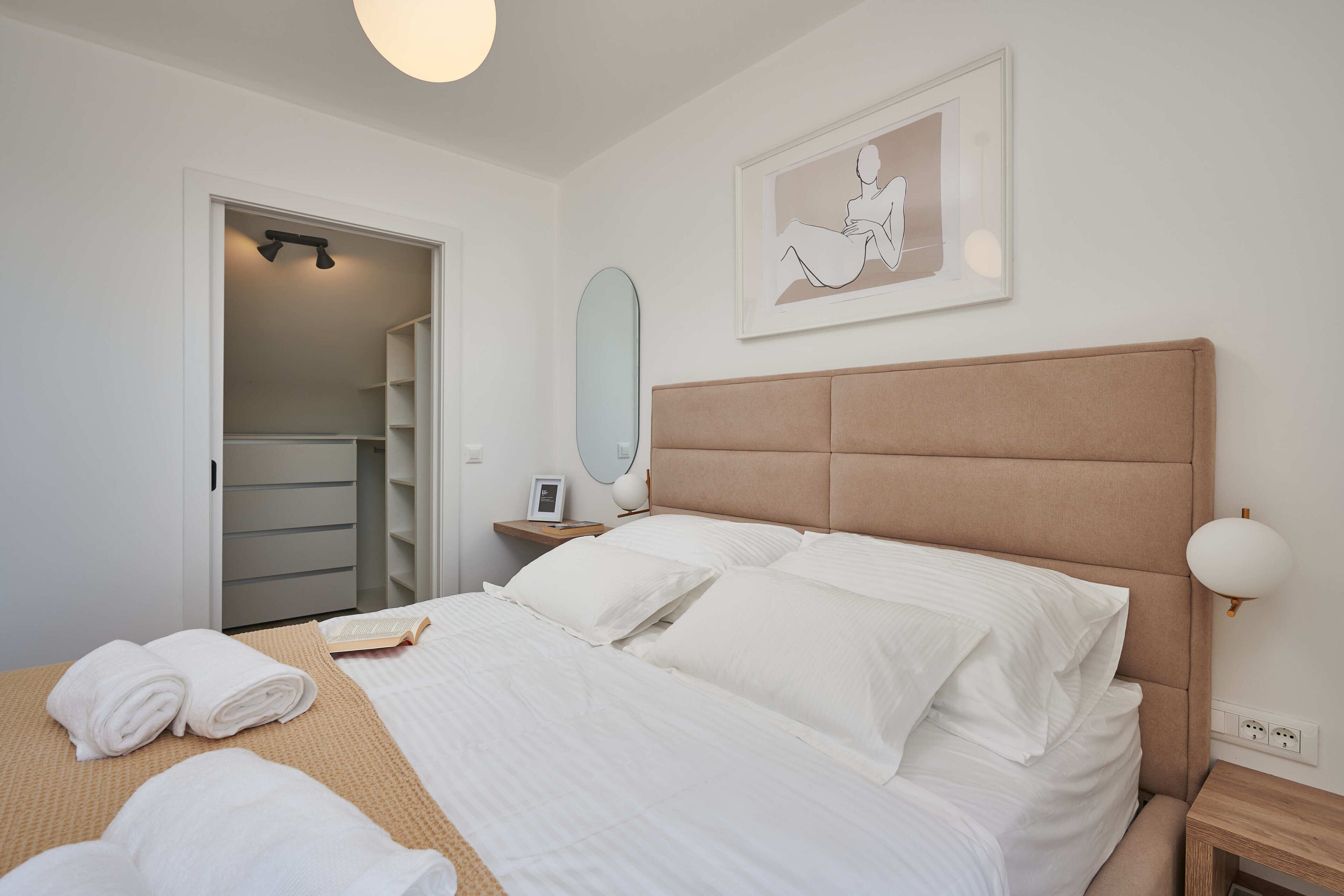 A neatly made bed with white linens, a bedside table with a lamp, and a framed artwork on the wall.