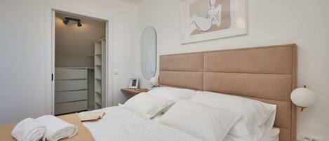 A neatly made bed with white linens, a bedside table with a lamp, and a framed artwork on the wall.
