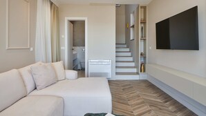A modern living room with a sofa, a flat-screen TV mounted on the wall, and a herringbone-patterned floor. - Apartment Blù (Dubrovnik)