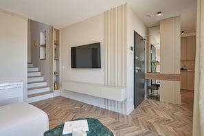 A modern hotel room with a flat-screen TV mounted on the wall, a built-in bench, a staircase, and a kitchenette area. - Apartment Blù (Dubrovnik)