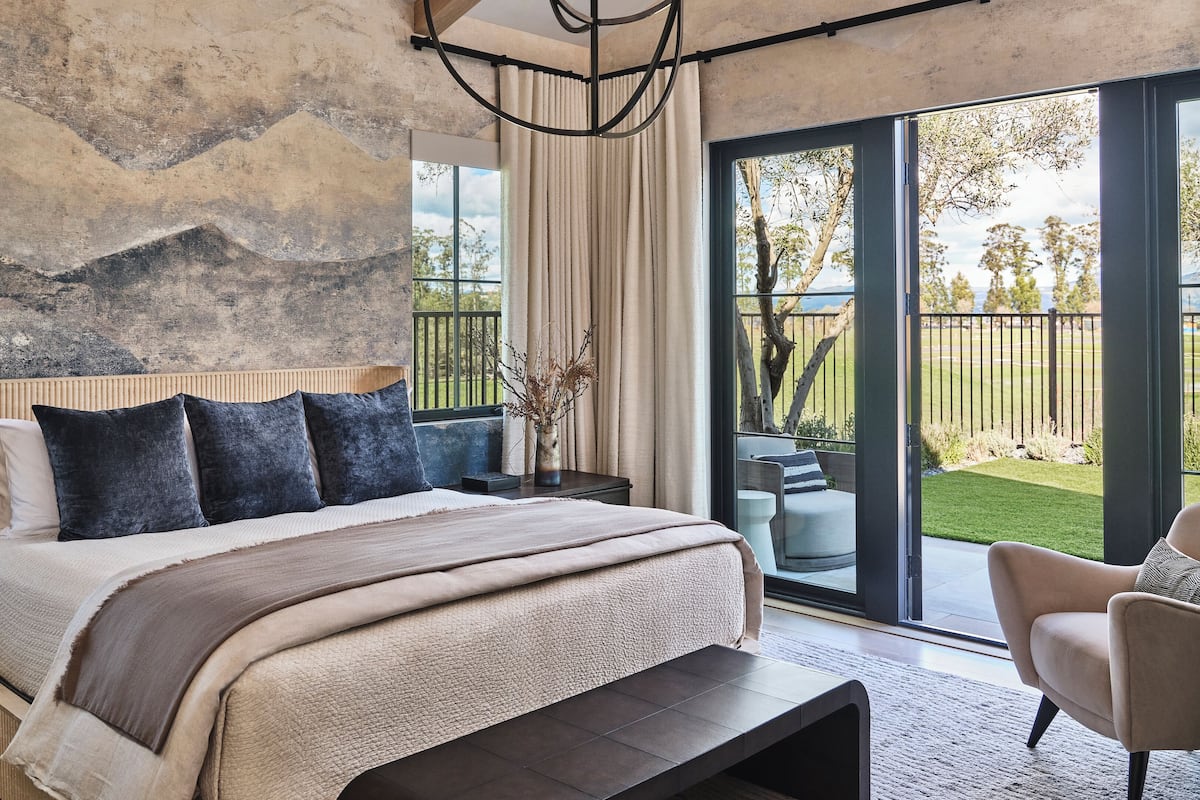 A modern bedroom with a large bed, a view of the outdoors, and a rustic wall.