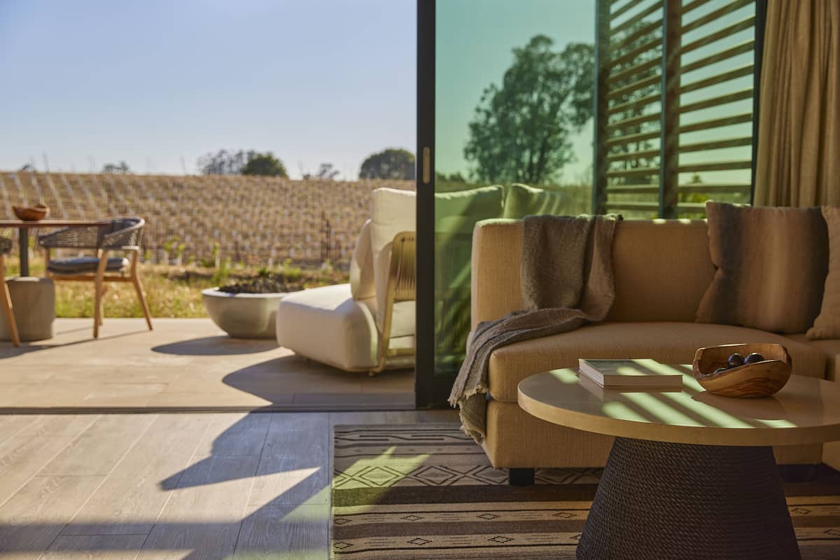 A modern living room with a sofa, a coffee table, and a view of a vineyard through large windows.