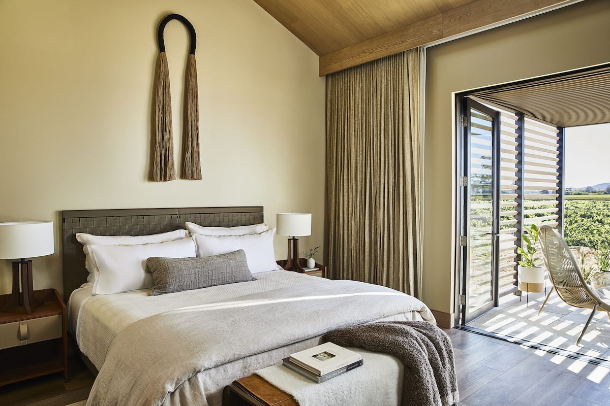 A neatly made bed with a grey and white duvet, a bedside lamp, and a book on the bedside table.