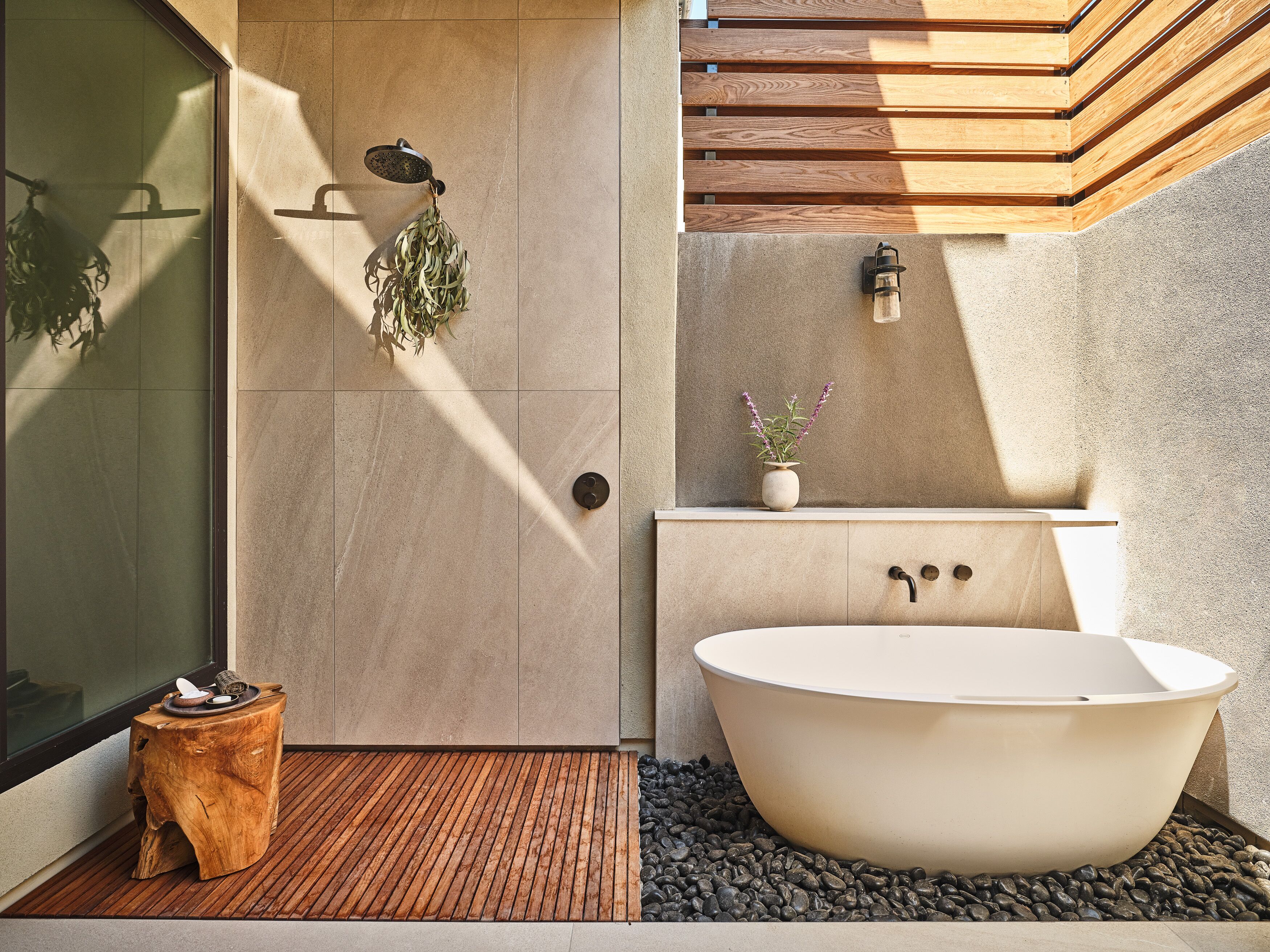 Un baño moderno con una bañera independiente, un banco de madera y una planta en maceta.
