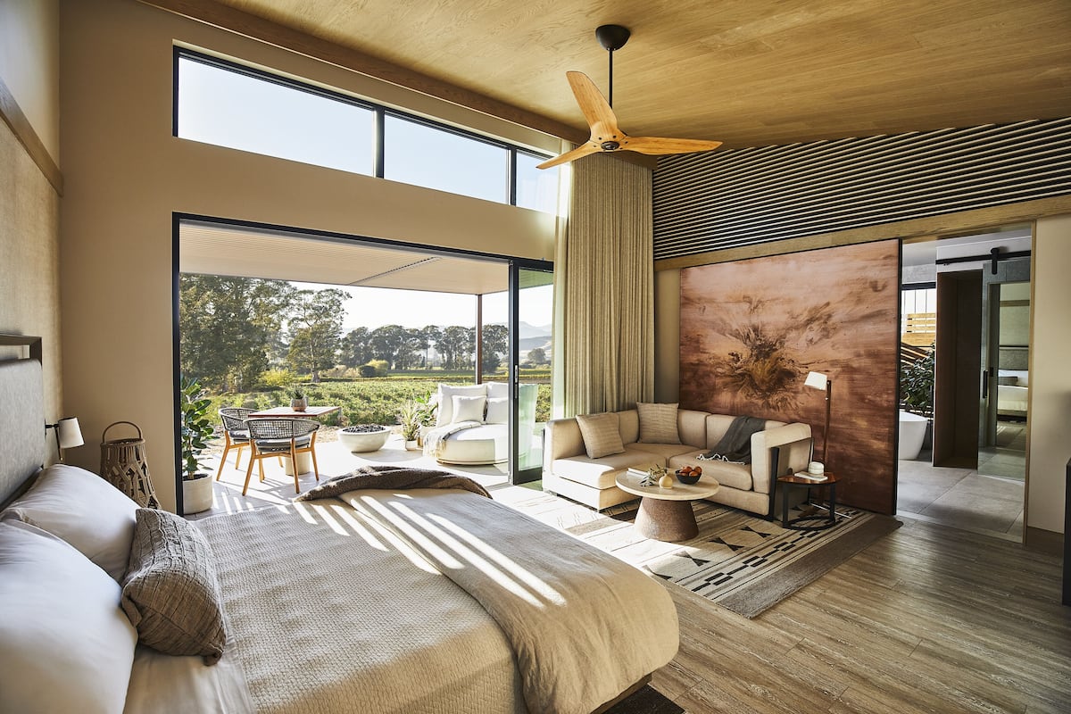 A spacious bedroom with a large bed, a ceiling fan, and a view of a garden through a sliding glass door.