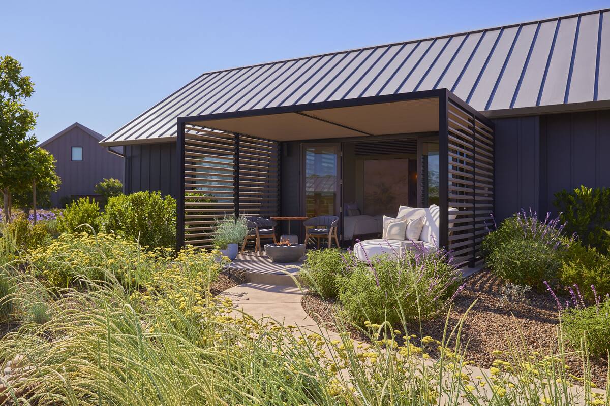 A modern house with a covered patio, outdoor seating, and a garden with various plants.