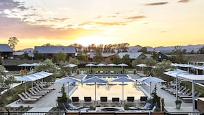 A poolside area with lounge chairs and umbrellas, surrounded by buildings and trees, during sunset. - Stanly Ranch, Auberge Collection (Napa)