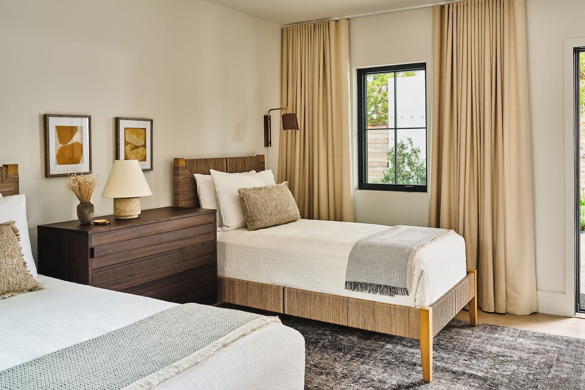 A bedroom with a bed, a dresser, a lamp, and a window with curtains.