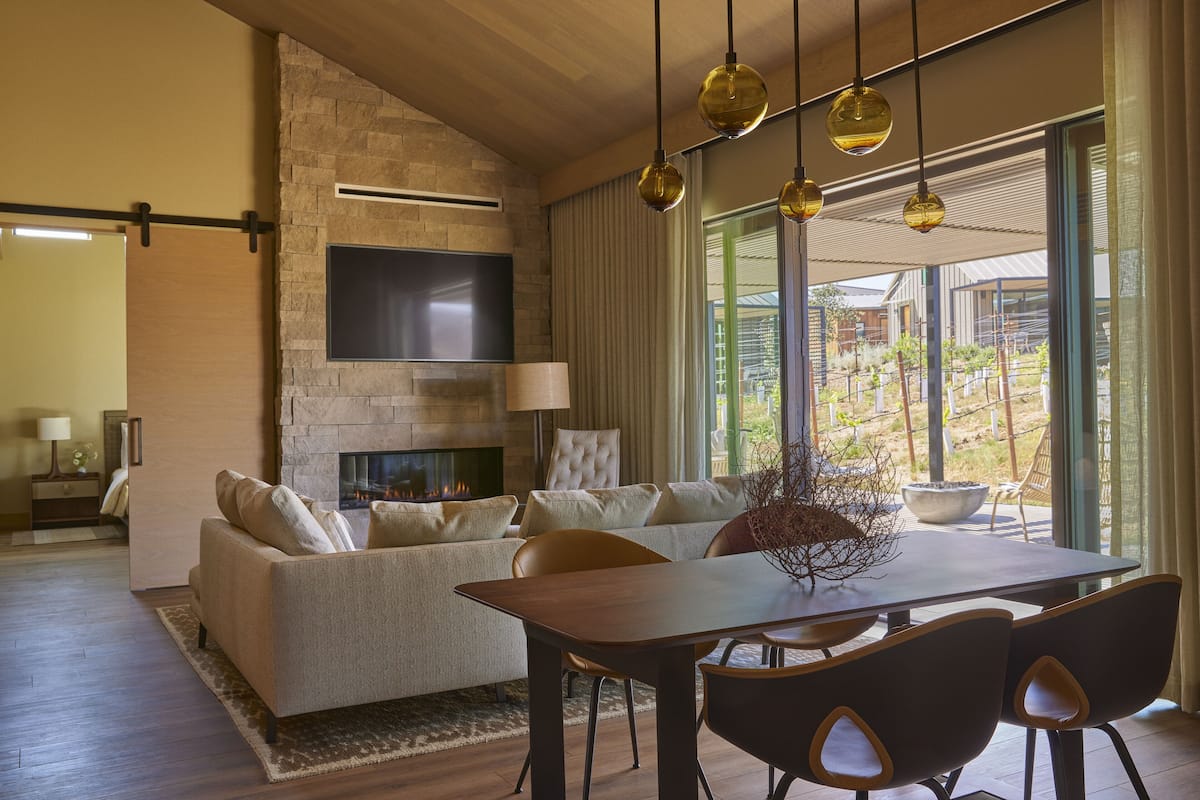 A modern living room with a stone fireplace, a sofa, a dining table, and a TV mounted on the wall.