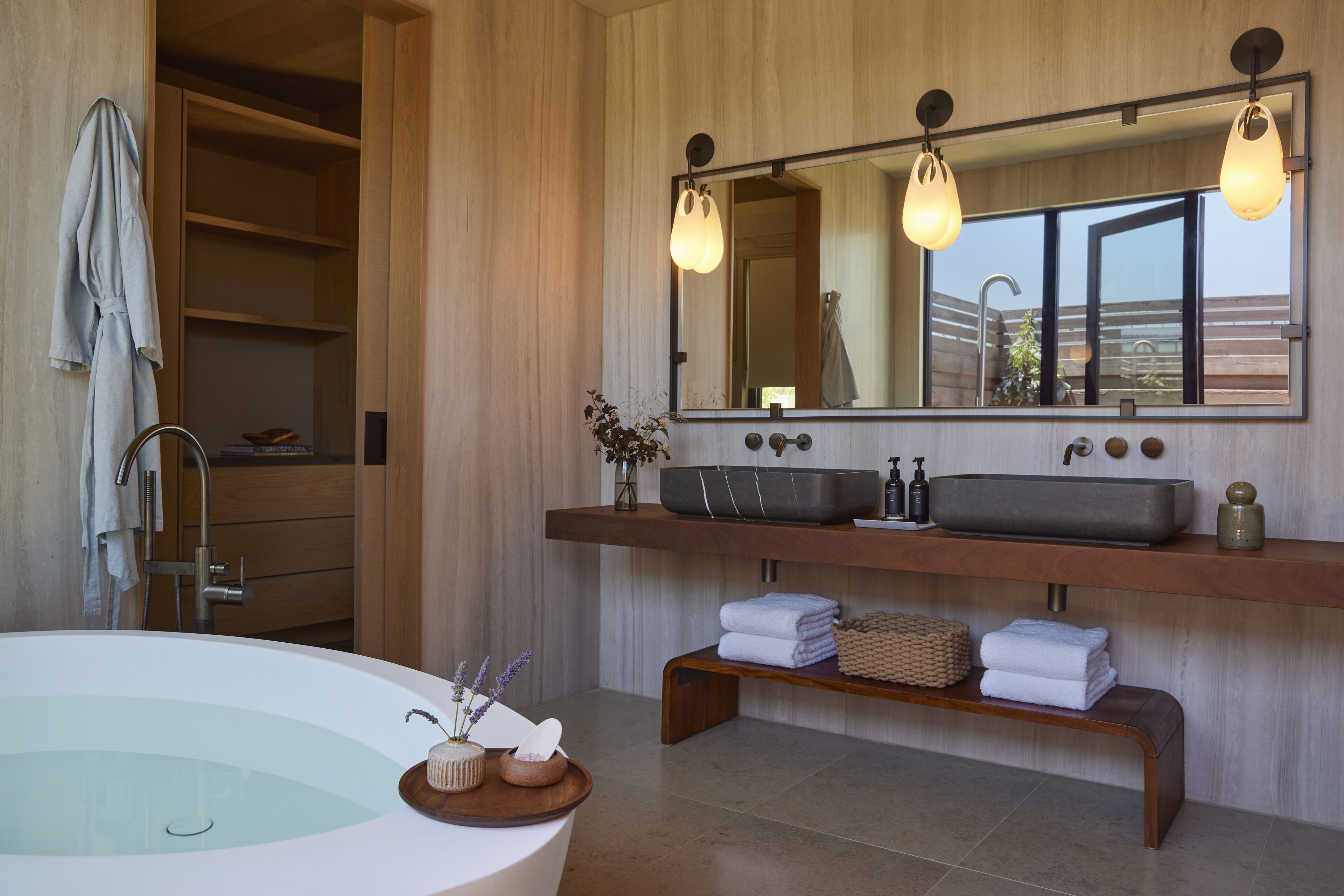A modern bathroom with a freestanding bathtub, a large mirror, and a wooden vanity with a sink and towel storage.