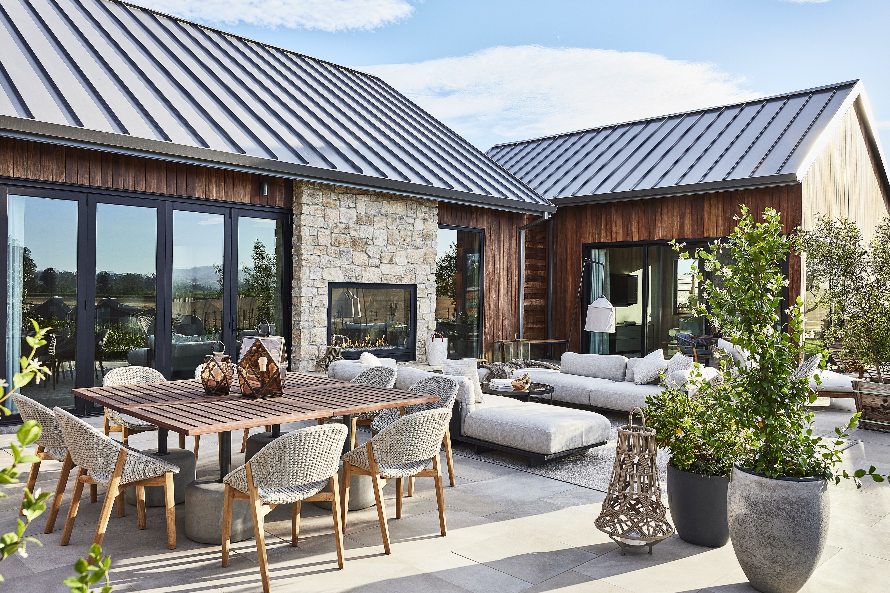 Un patio moderno al aire libre con chimenea de piedra, muebles de madera y plantas en macetas.