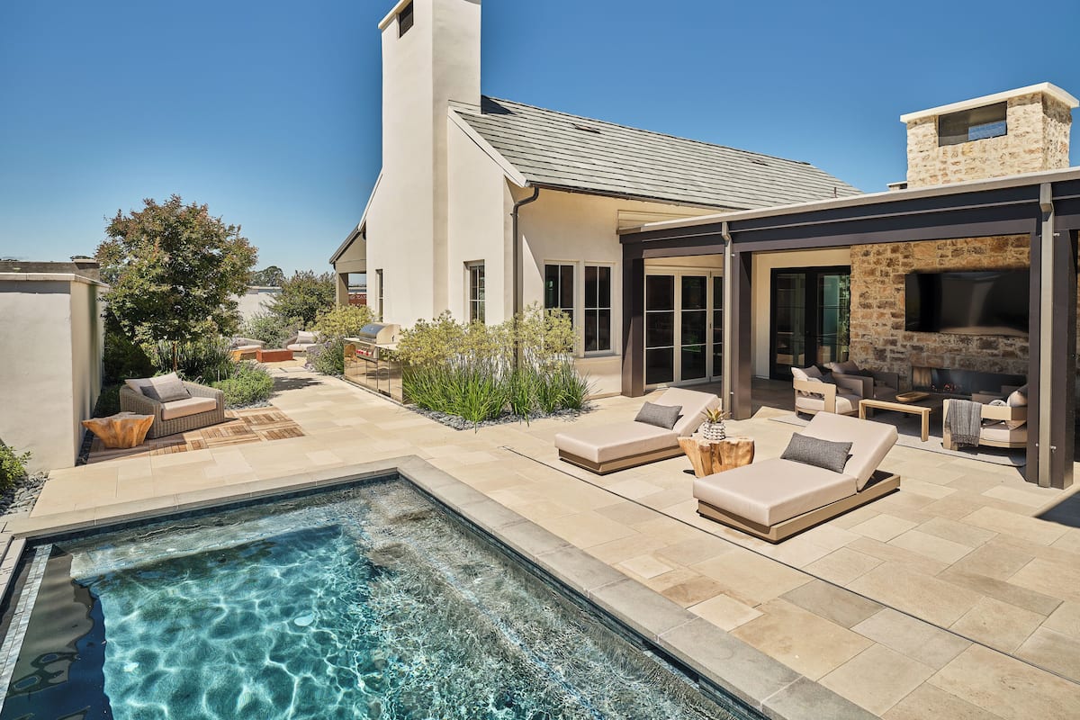 A modern outdoor living area with a pool, outdoor seating, and a stone fireplace.