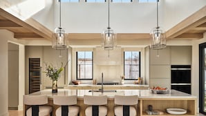 A modern kitchen with a central island, bar stools, pendant lights, and a view of the outdoors. - Stanly Ranch, Auberge Collection (Napa)