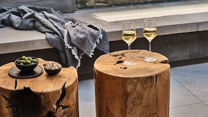 A cozy outdoor seating area with two wooden stools and a bench, a bowl of olives, and a glass of white wine. - Stanly Ranch, Auberge Collection (Napa)