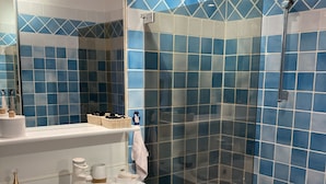 Een badkamer met een wit wastafelmeubel, een douchecabine van glas en blauwe betegelde wanden.