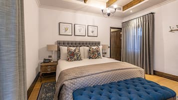 Quarto com cama grande, um banquinho azul estofado, mesa de cabeceira de madeira e mesa lateral com abajur.