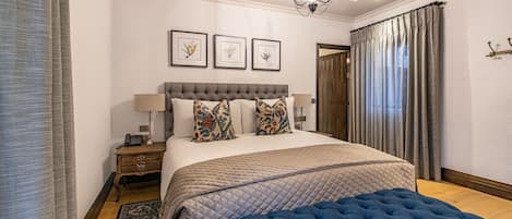 A bedroom with a large bed, a blue upholstered bench, a wooden nightstand, and a bedside table with a lamp.