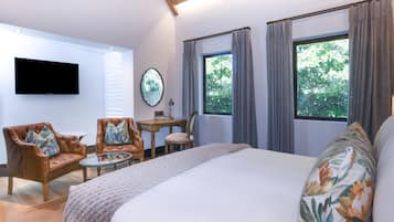 A hotel room with a large bed, a flat-screen TV mounted on the wall, a small round table with chairs, and a window with curtains.