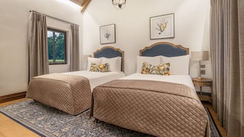 Una habitación doble con dos camas, un ventanal grande, una araña y una alfombra estampada.
