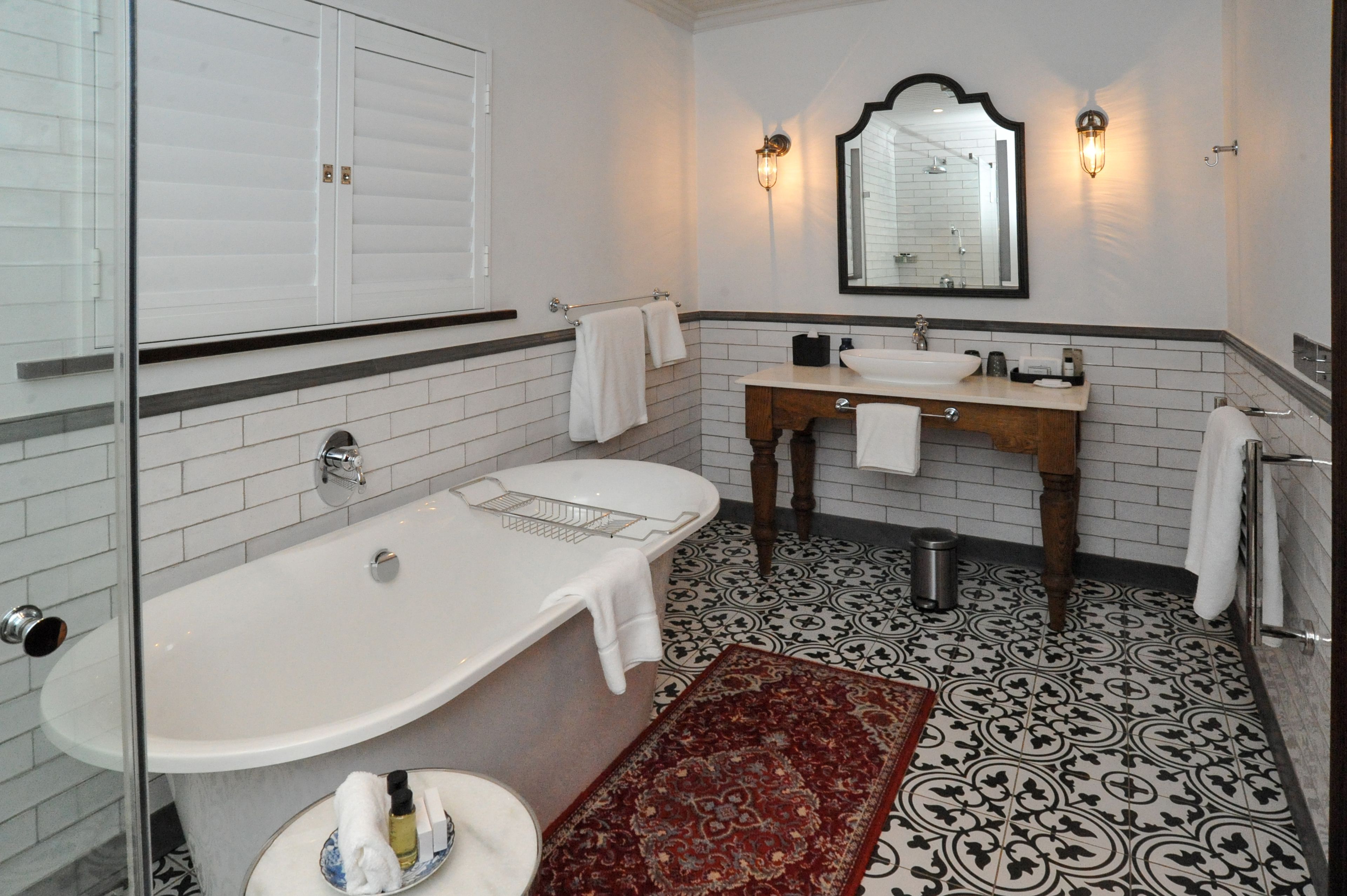 Un baño con una bañera blanca, un tocador de madera con espejo y baldosas de suelo con diseño.