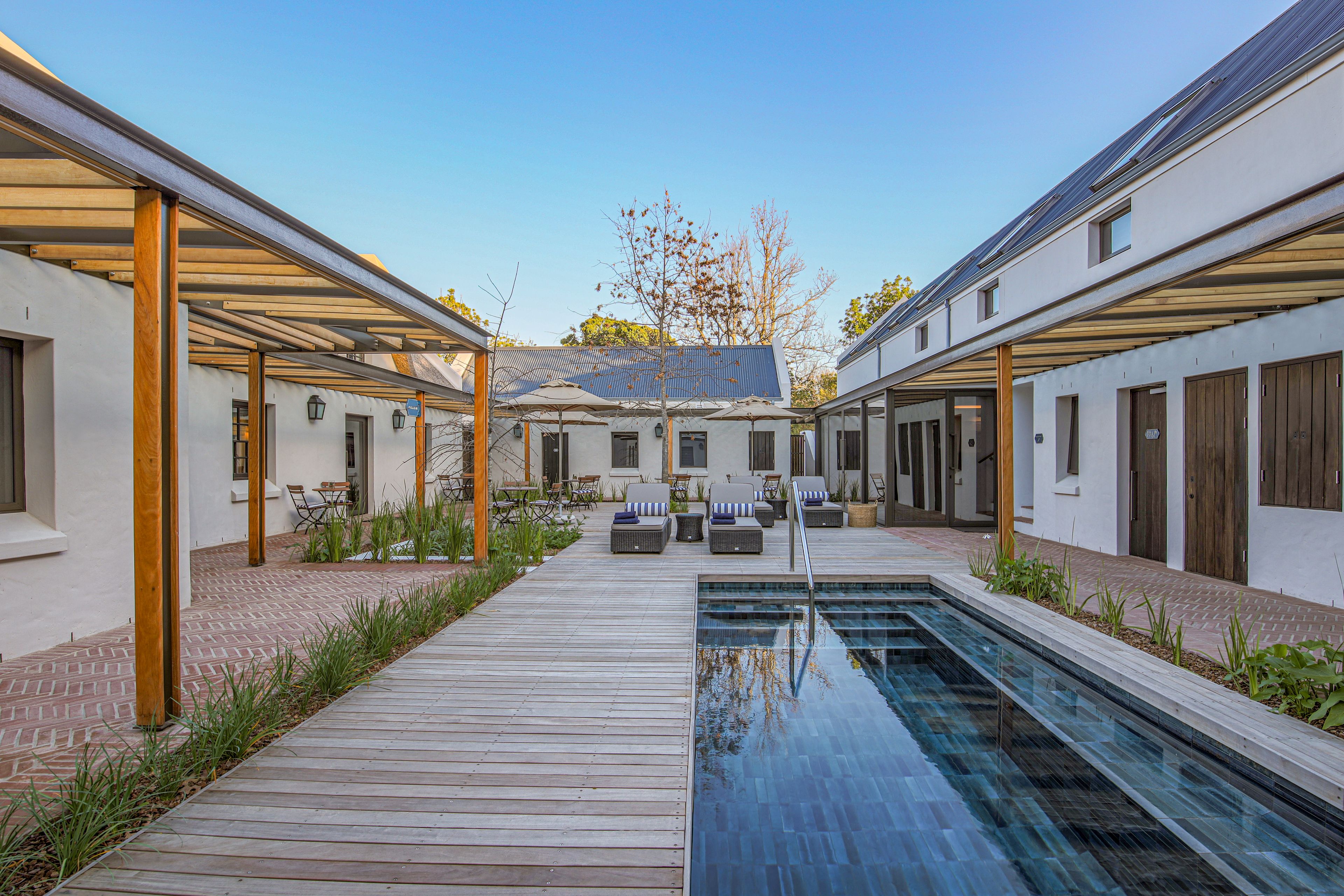 A modern outdoor pool area with a wooden deck, lounge chairs, and a clear blue pool.