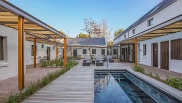 A modern outdoor pool area with a wooden deck, lounge chairs, and a clear blue pool.