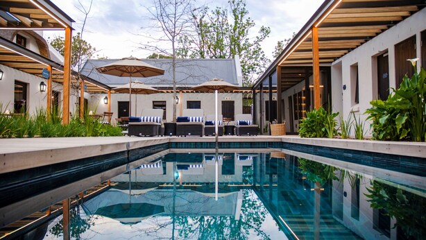 A modern pool area with lounge chairs and umbrellas, surrounded by greenery and architectural features.