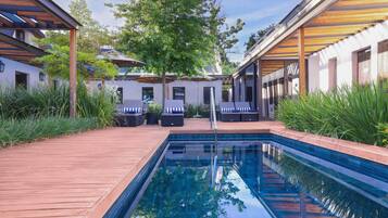 A swimming pool with a wooden deck, lounge chairs, and a covered seating area.