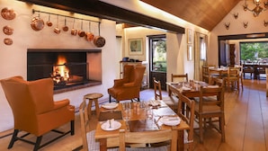 A dining area with wooden tables and chairs, a fireplace, and a view of the outdoors.