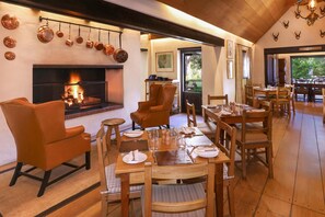 Un espace repas avec des tables et des chaises en bois, une cheminée et une vue sur l’extérieur.