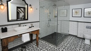A modern bathroom with a white sink, wooden vanity, a glass shower enclosure, and patterned floor tiles.