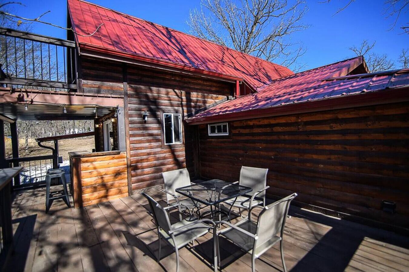 Eine Holzhütte mit rotem Dach, einer Terrasse mit Gartenmöbeln sowie einem Metalltisch und Stühlen.
