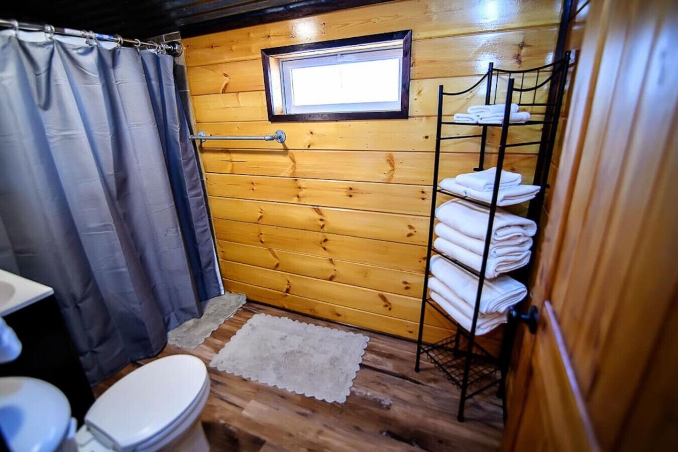 Un baño de cabaña de madera con un inodoro, una cortina de ducha, una ventana y un perchero para toallas.
