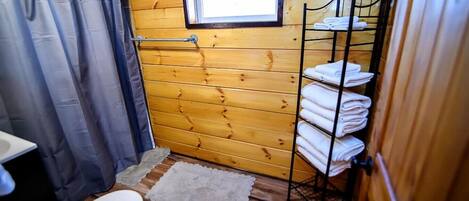 Un baño de cabaña de madera con un inodoro, una cortina de ducha, una ventana y un perchero para toallas.