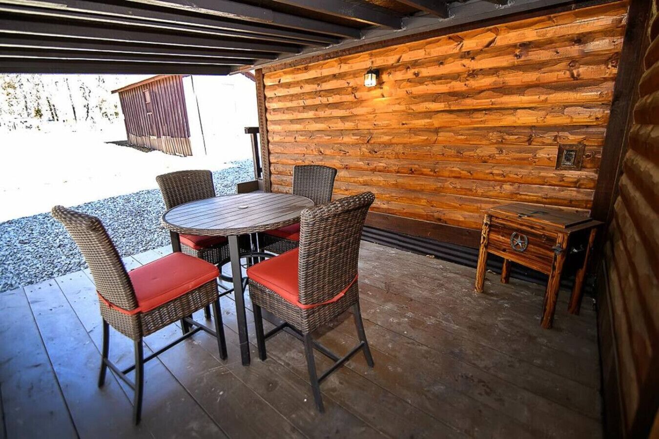Un espacio de patio techado con una mesa redonda y sillas de mimbre con cojines rojos.