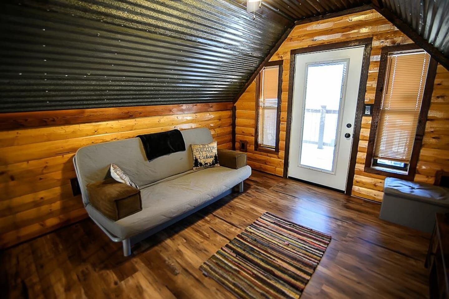 L’intérieur d’un chalet confortable, avec un canapé, un tapis à motifs et une porte donnant sur l’extérieur.
