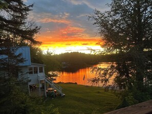 Una casa con terraza y vista a un lago al atardecer.