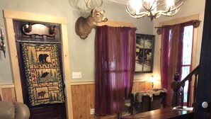 A cozy living room with a leather sofa, a glass coffee table, a wooden dining table, and a deer head mounted on the wall.