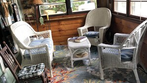 A cozy room with wicker furniture, a colorful rug, and a view of the outdoors through large windows.