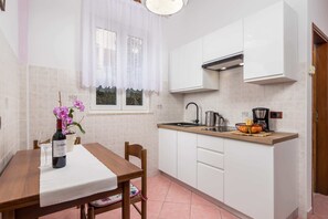Et køkken med hvide skabe, en træbordplade, en vask, en komfur og et vindue med et hvidt gardin.