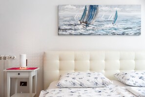 Et soveværelse med en seng, et natbord med en lampe, og et maleri af sejlbåde på væggen.