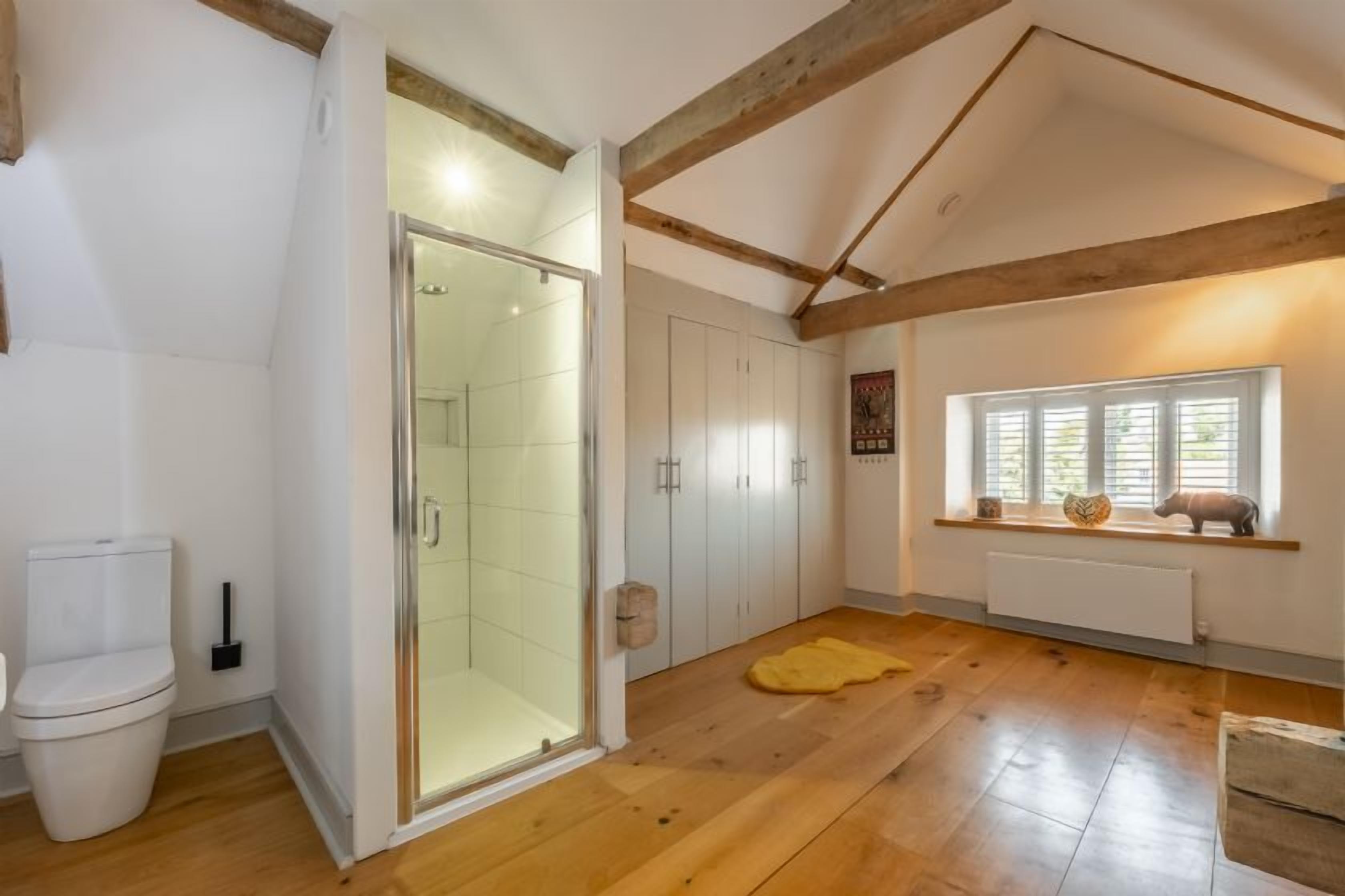 A spacious room with a wooden floor, a glass shower enclosure, white cabinets, and a window with a view.