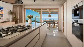 A modern kitchen with a central island, a dining area with a view of the sea, and a built-in Bosch oven.