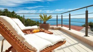 A balcony with a wooden chair, a table with breakfast items, and a potted plant.