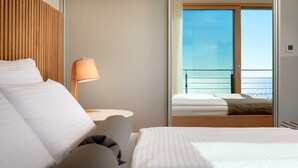 A hotel room with a bed, a nightstand, a lamp, and a view of the sea through a balcony.